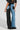 Rear view of a person wearing stylish EXTREME STRETCH PATCHWORK WIDE LEG JEANS, featuring one black leg and one blue leg in stretch denim, showcasing multiple pockets and intricate stitching. The unique design complements a black graphic t-shirt and matching shoes.