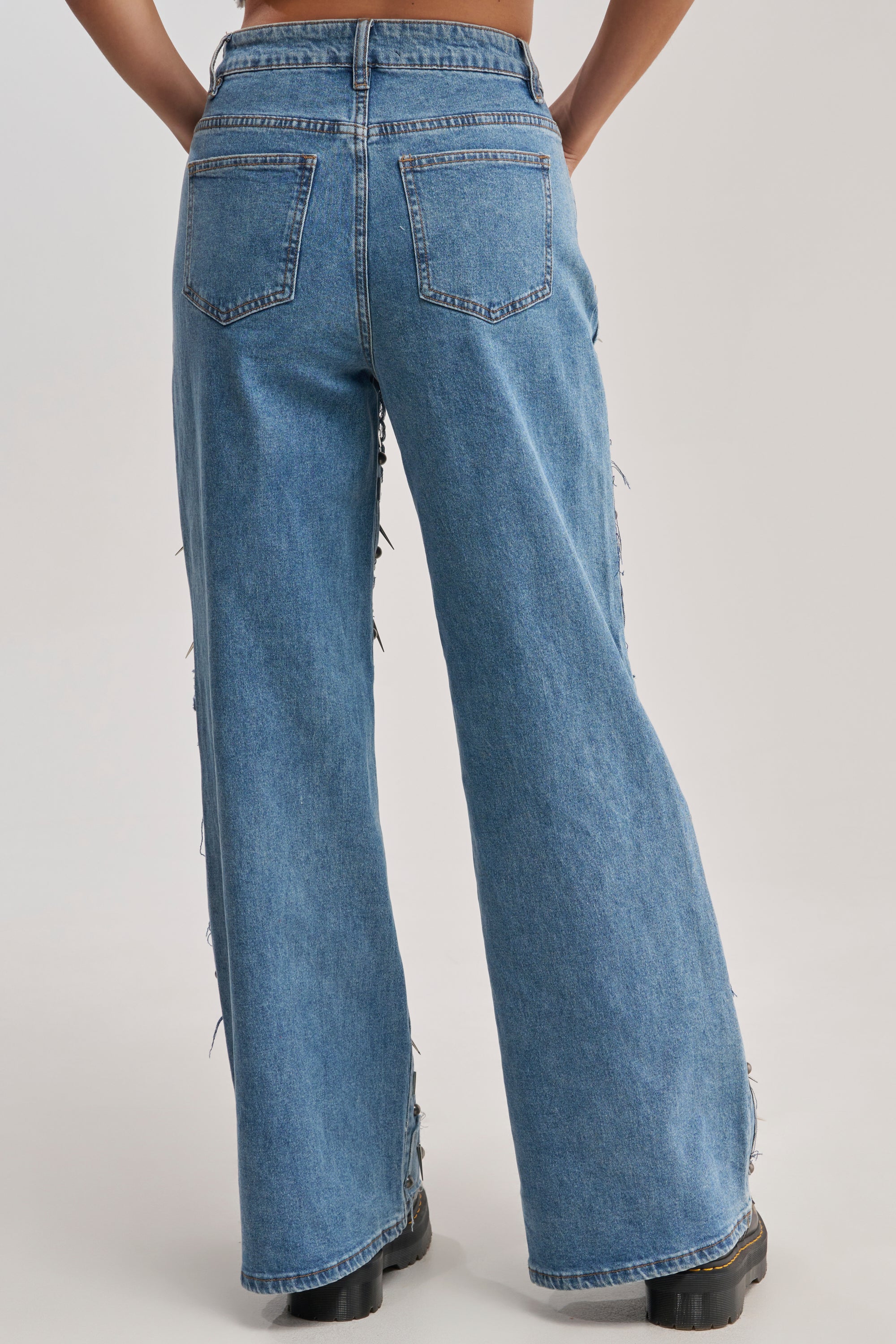 A person is shown from the back against a plain, light background wearing MIXED EMOTIONS EMBELLISHED DENIM and black boots.