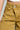 Close-up of a person wearing the GIVE IT TO ME LOW RISE DENIM PANT, featuring a mustard-colored corduroy finish with two visible buttons and a flared silhouette. The top of a white shirt is just visible as the person's left hand rests near the pocket.