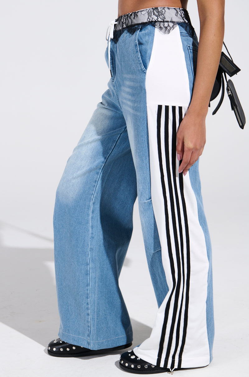 Only the lower half is shown, featuring SPORTY AND SWEET LIGHT WASH DENIM TRACK PANTS with white side panels and black vertical stripes, styled with a black-and-white snakeskin belt and black studded shoes for streetwear flair.