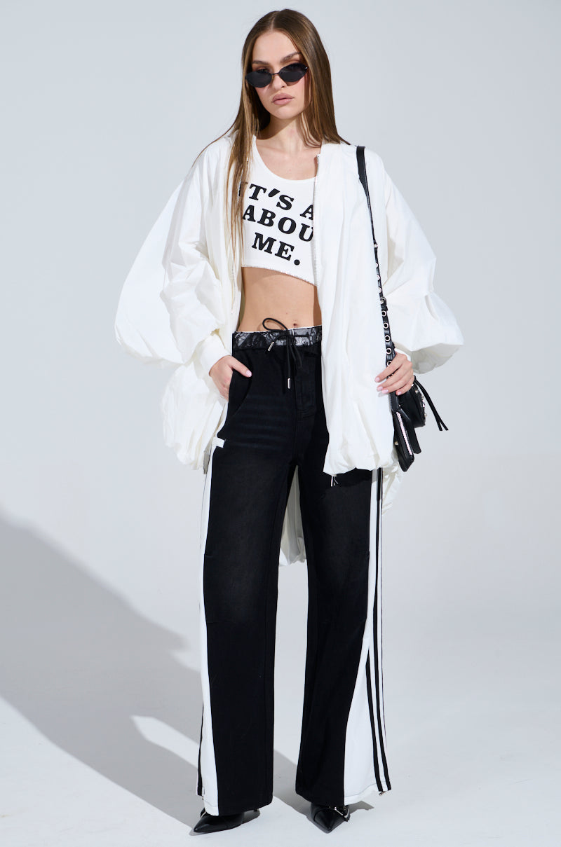 Rocking a white oversized jacket and chilled sunglasses, they effortlessly pair a sporty-chic white crop top with the Sporty and Sweet Black Wash Denim Track Pants. With a sleek black purse in hand, they strike a perfect balance of style against an unadorned backdrop.