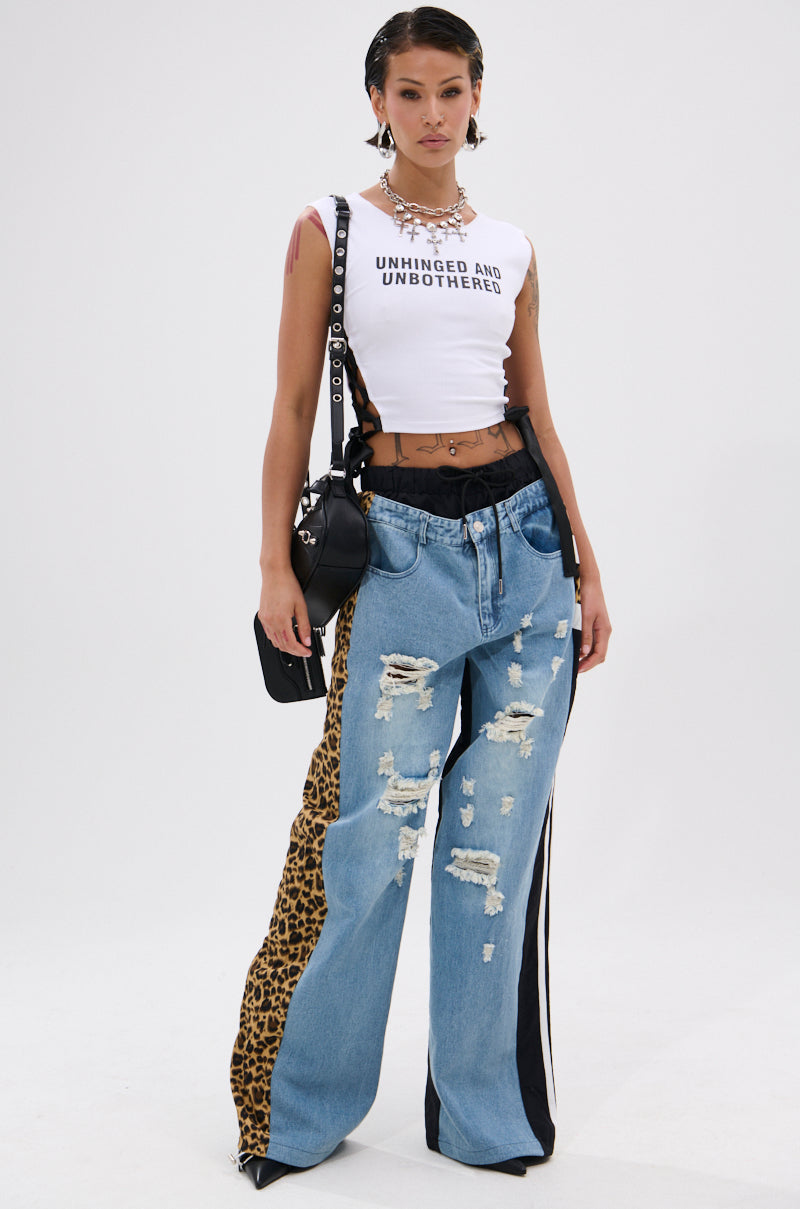 A woman poses against a white background, wearing WILDIN' OUT DENIM TRACKPANTS with leopard-print panels, a white "UNHINGED AND UNBOTHERED" crop top, a black belt, black purse, and layered necklaces. 6