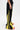 A person models the GAME TIME DECISION DENIM PANT—black wide-leg jeans with bold yellow panels and three vertical yellow stripes—paired with red and white sneakers, shown from the waist down against a plain white background.