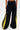 A person is seen from the back wearing GAME TIME DECISION DENIM PANT—black wide-leg streetwear jeans featuring bright yellow panels and black side stripes—against a plain white background.