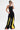 A person stands confidently against a white background wearing oversized green goggles, a black sleeveless bodysuit, and the GAME TIME DECISION DENIM PANT—high waist wide-leg jeans with bold yellow panels—paired with red-soled shoes.