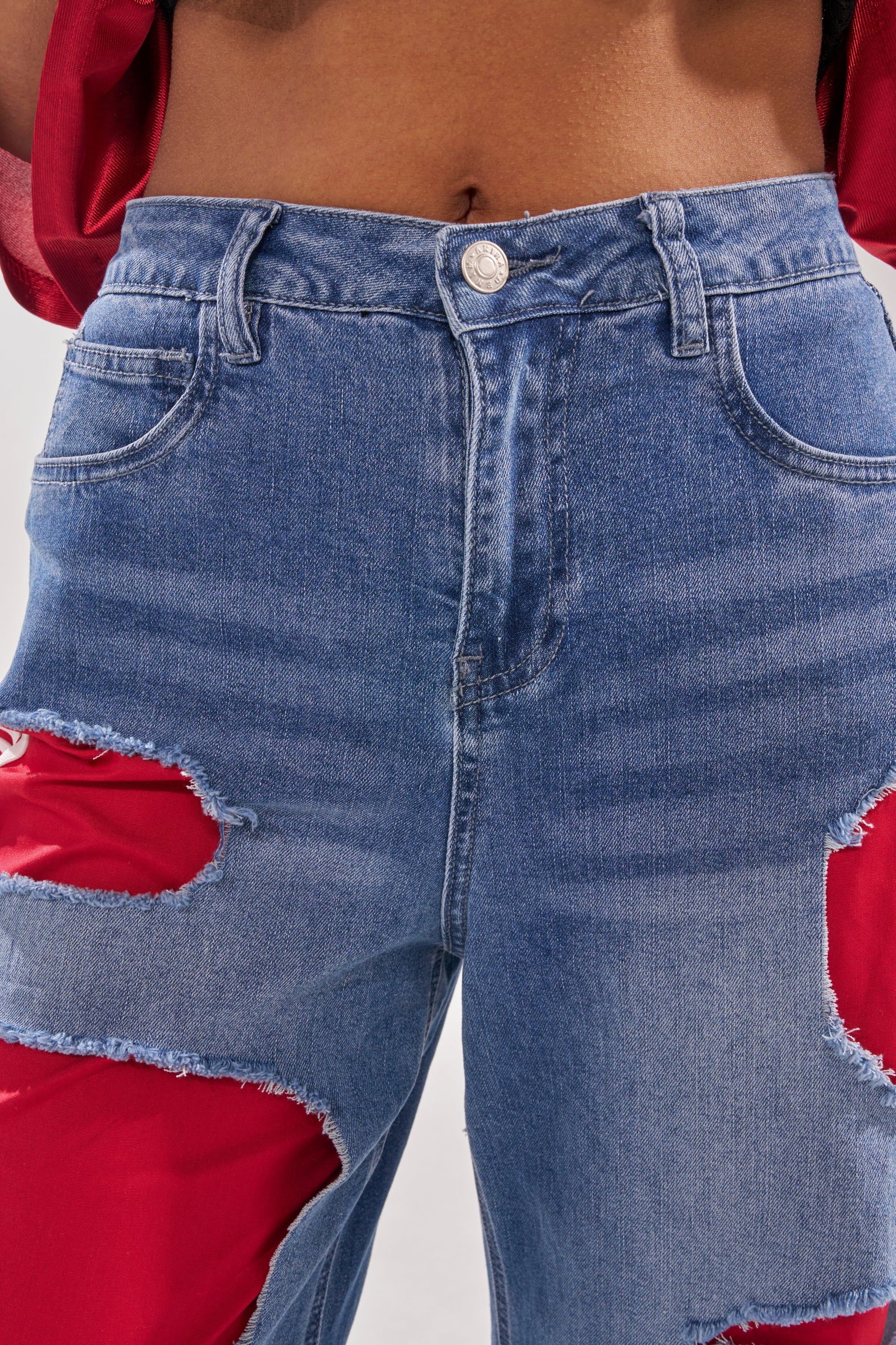 Close-up of a person wearing the LEXIE LOW RISE DENIM TRACK PANT featuring wide legs and bold distressed patches with red fabric underneath, paired with a red top. Only the torso and upper legs are shown—ideal for Y2K streetwear fans. 7