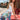 A woman with long wavy hair wears the KISS MY PATCH DENIM SHORT and a white tank top, posing by a red picnic table on a sunny city street.