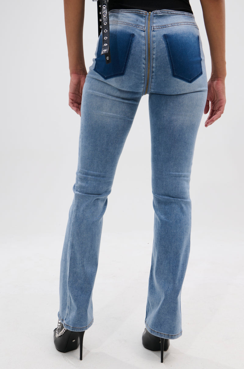 A person stands facing away on a white background wearing TOO GOOD TO BE TRUE LOW RISE DENIM FLARE PANT in light blue with a back zipper and dark blue pockets, paired with black high-heeled shoes.