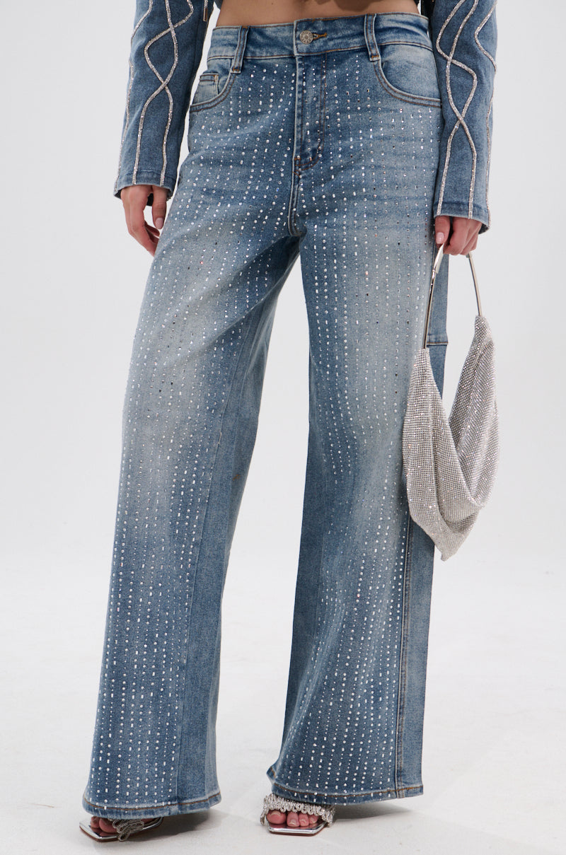 Wearing the SPARKLE SHINE DENIM PANT with vertical rhinestone embellishments, matched with a coordinating jacket, open-toe heels, and a small sparkly silver handbag.
