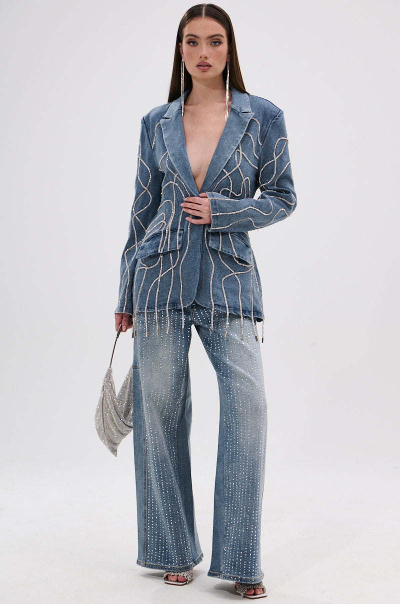 A woman wears the SPARKLE SHINE DENIM PANT with a light blue denim blazer featuring white wavy lines and beads, styled with a silver bag and heeled sandals against a plain background.