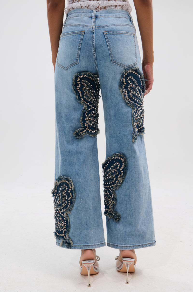 A person wearing REBIRTH BUTTERFLY PATCH JEANS featuring light blue wide legs, dark denim, and pearl swirl embellishments, paired with high-heeled pointed-toe shoes. The photo is taken from behind against a plain background. 4