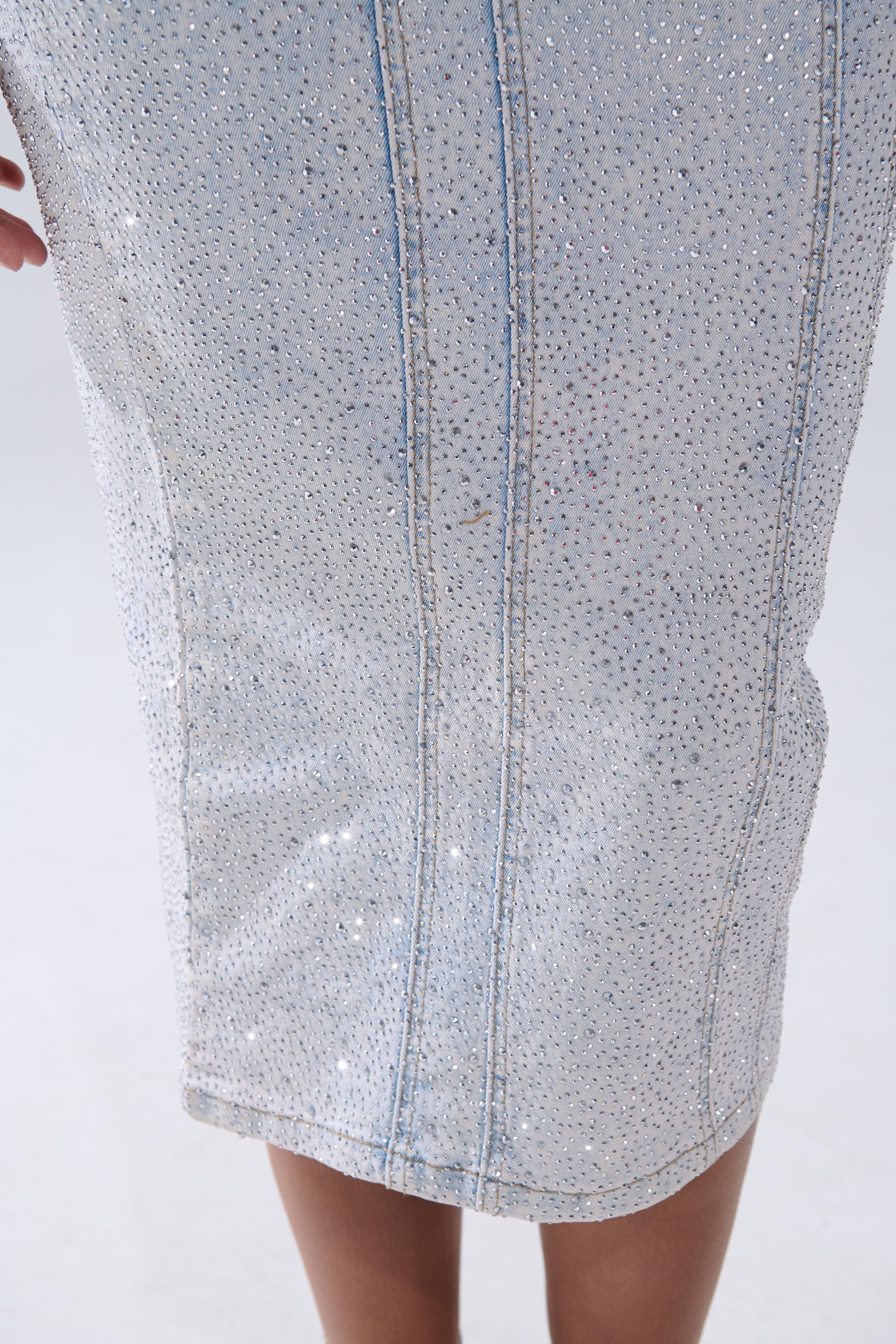 A close-up of a person wearing the AFTER HOURS DENIM RHINESTONE MIDI DRESS, a light blue midi dress adorned with sparkling rhinestones and vertical seams for a chic party look.