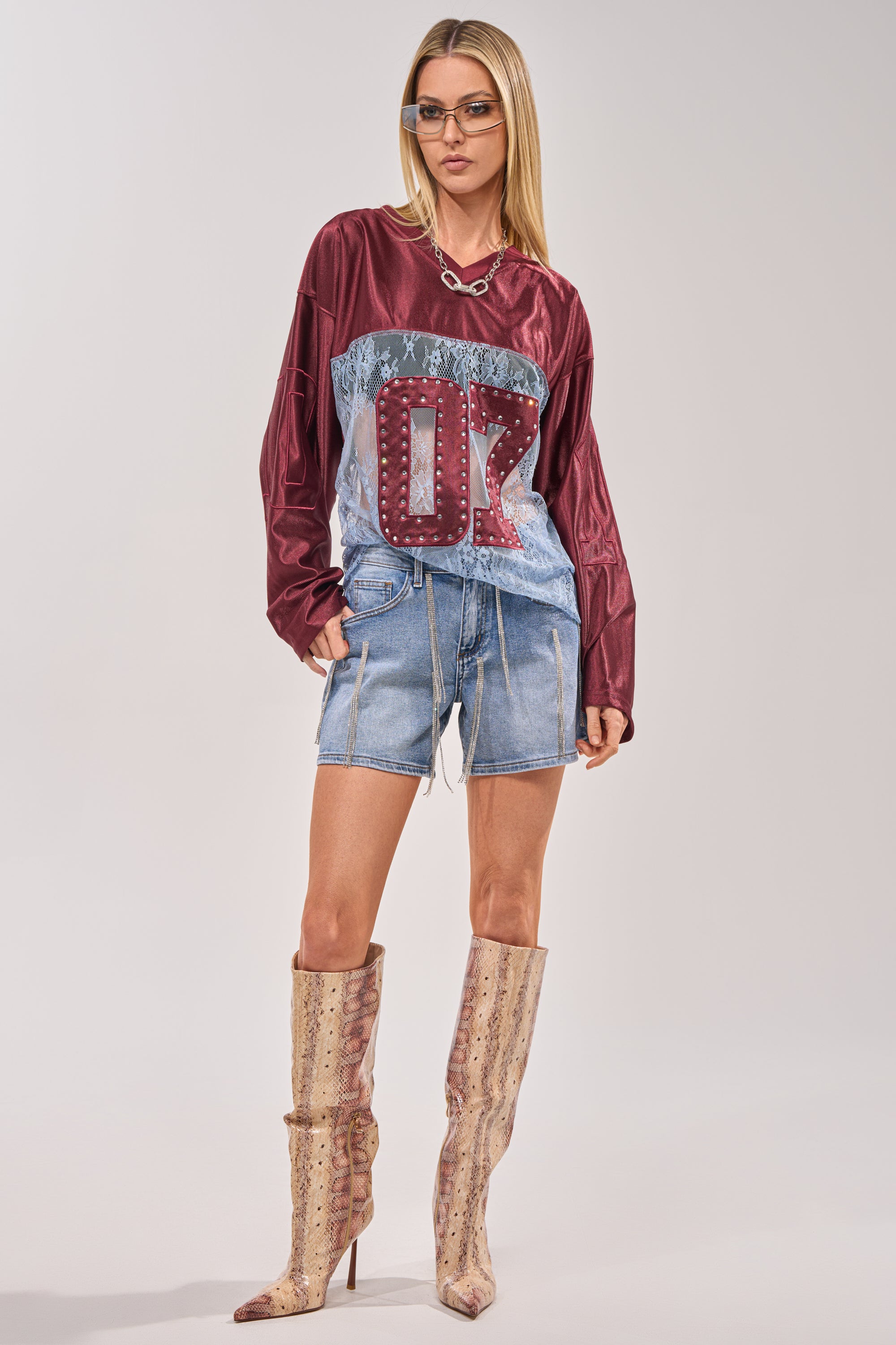 A woman in sunglasses, a maroon and blue jersey with "00," DRIP CITY DENIM SHORTS with rhinestone fringe, and knee-high snakeskin boots stands confidently against a plain background. 4