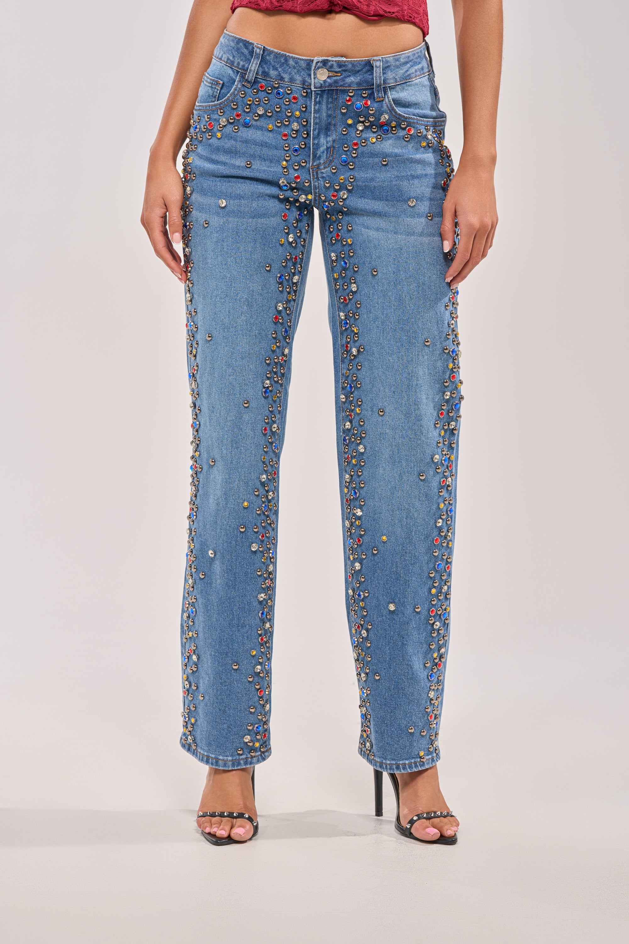 A person wearing the JESSIE RHINESTONE DENIM, featuring dark-wash rhinestone-studded straight-leg jeans and high-heeled sandals, shown from the waist down against a plain background. 2