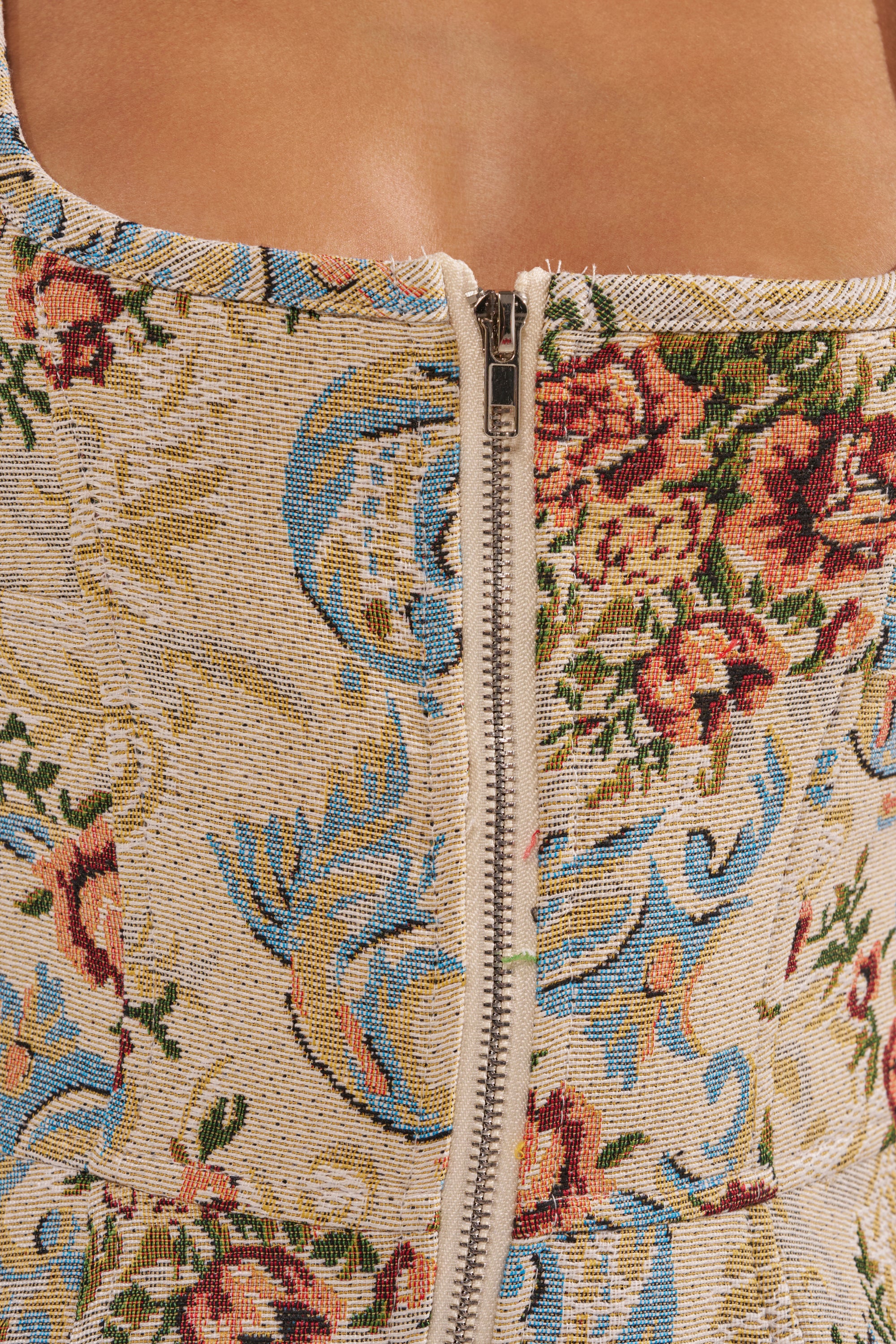 Close-up of the MATCH POINT MINI DRESS IN LIGHT BROCADE, featuring a central zipper and an intricate floral and bird tapestry pattern in red, green, blue, and gold on beige. 7