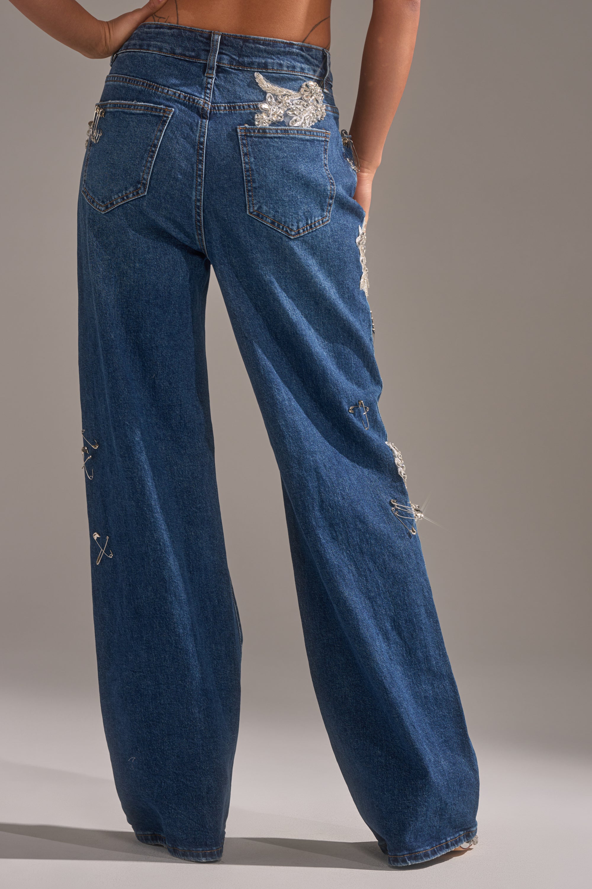 A person is shown from the back wearing LETS GO BABY DISTRESSED DENIM—wide-leg, high-waisted blue jeans with silver embellishments and distressed details—against a plain background. 4