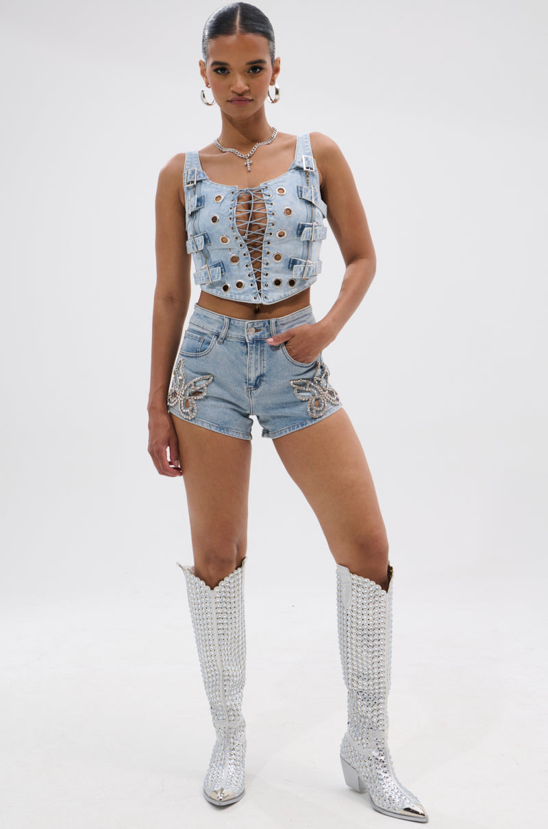 A woman stands confidently in a lace-up denim crop top, BUTTERFLY QUEEN DENIM SHORT, and tall silver studded cowboy boots against a plain white background. 6
