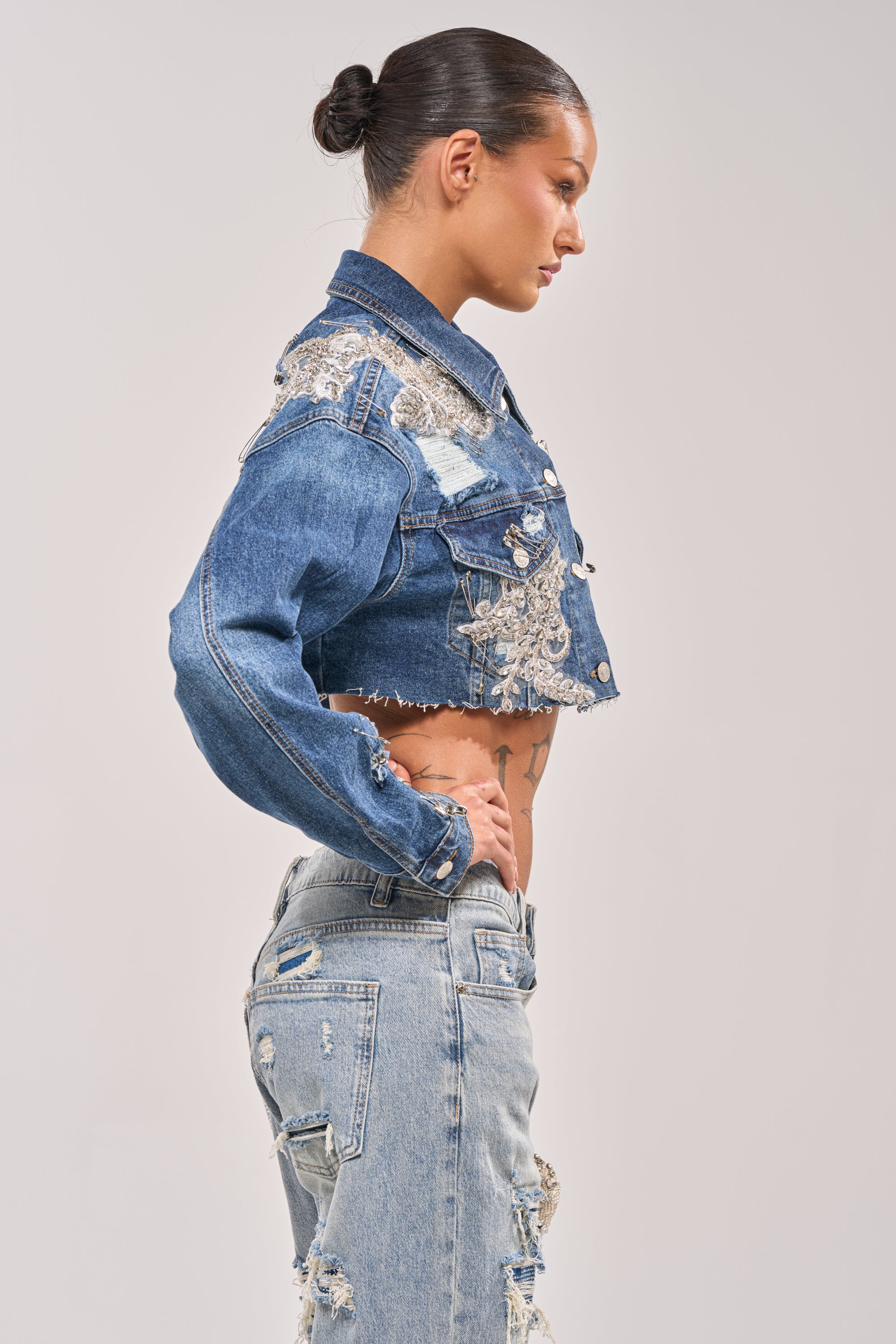 A woman in profile wears the LET'S RIDE EMBELLISHED DENIM JACKET with rhinestone clusters and distressed high-waisted jeans. Her hair is pulled into a sleek bun, set against a plain light gray background. 4