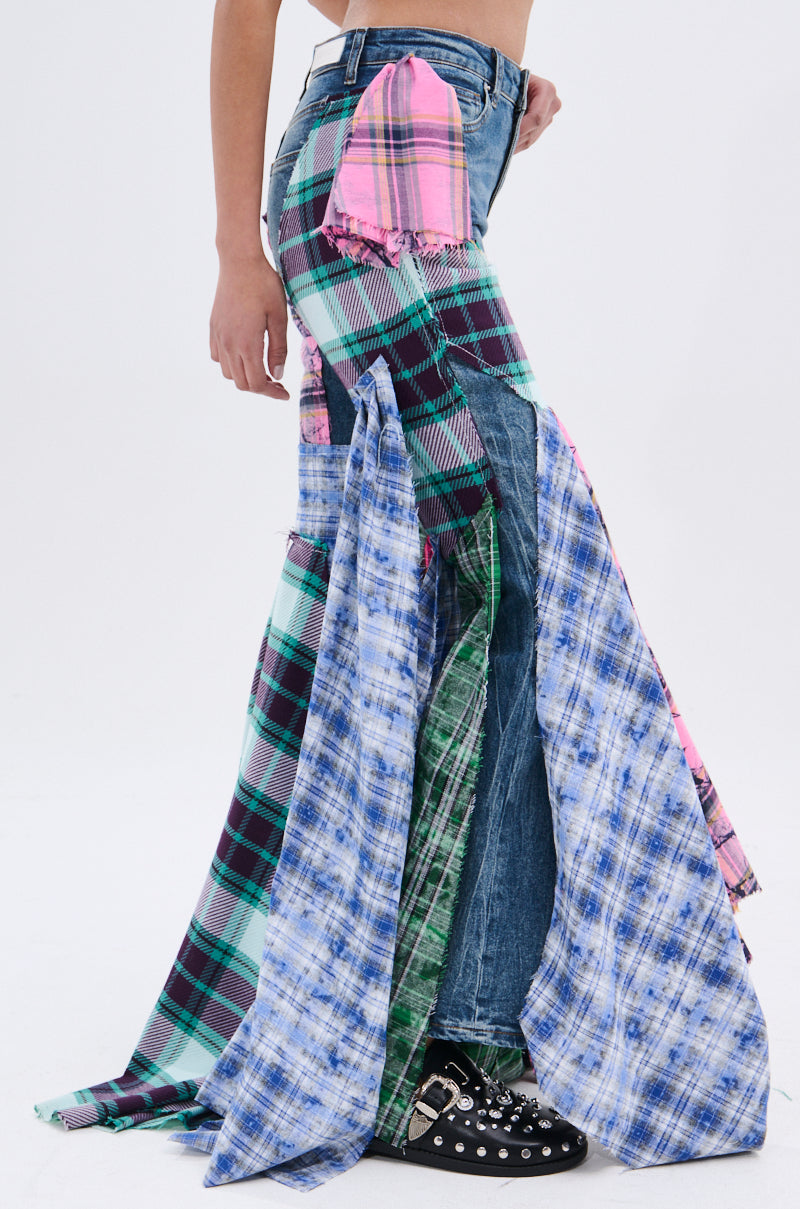 A person models PLAID ON PLAID DENIM JEANS with large blue, green, pink, and purple plaid patchwork panels, paired with studded black shoes. The cropped image shows the outfit from waist to feet against a plain background.