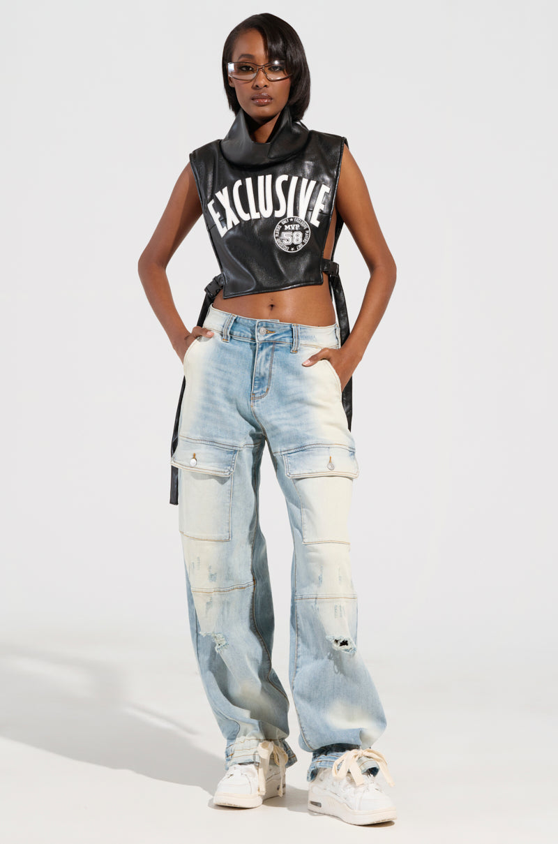 A person wearing sunglasses, a black sleeveless top with "Exclusive" written on it, and FOREVER AND A YEAR DENIM JEANS in light blue with a wide-leg silhouette. They are standing on a plain white background, paired with white sneakers.