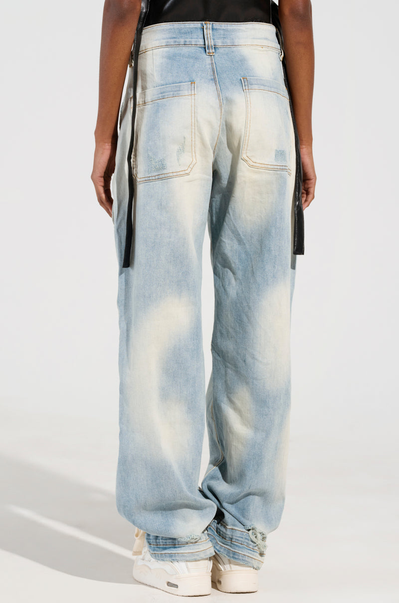 A person is wearing the FOREVER AND A YEAR DENIM JEANS, featuring a loose fit and high-rise design with a faded denim effect and visible stitching. The wide-leg silhouette includes two back pockets and black straps hanging at the sides. They are standing on a light surface.