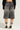 A person sporting the LITERAL PERFECTION black denim Bermuda shorts stands with their back to the camera. Complementing their look, they wear a black sweater and high-top sneakers with thick white laces, effortlessly blending comfort and style.