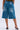 A person in LITERAL PERFECTION BLUE DENIM BERMUDA SHORTS—knee-length, baggy fit with wide legs, raw hems, and back pockets—is paired with high-heeled open-toe shoes against a plain background.