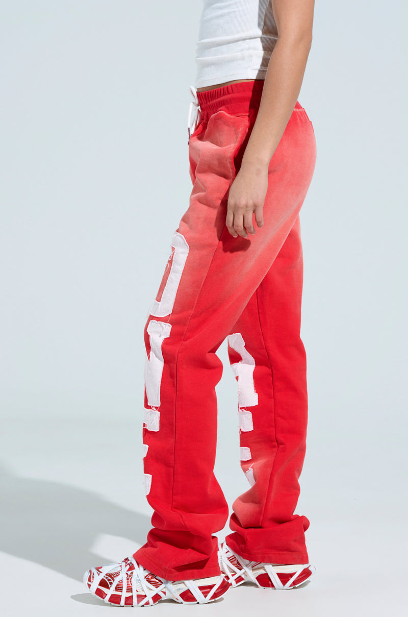The person is wearing ONLY ONE WIDE LEG PANT in red with an elastic waistband and large white text on the side, paired with a white tank top and red-white geometric sneakers, against a light gray background. 4