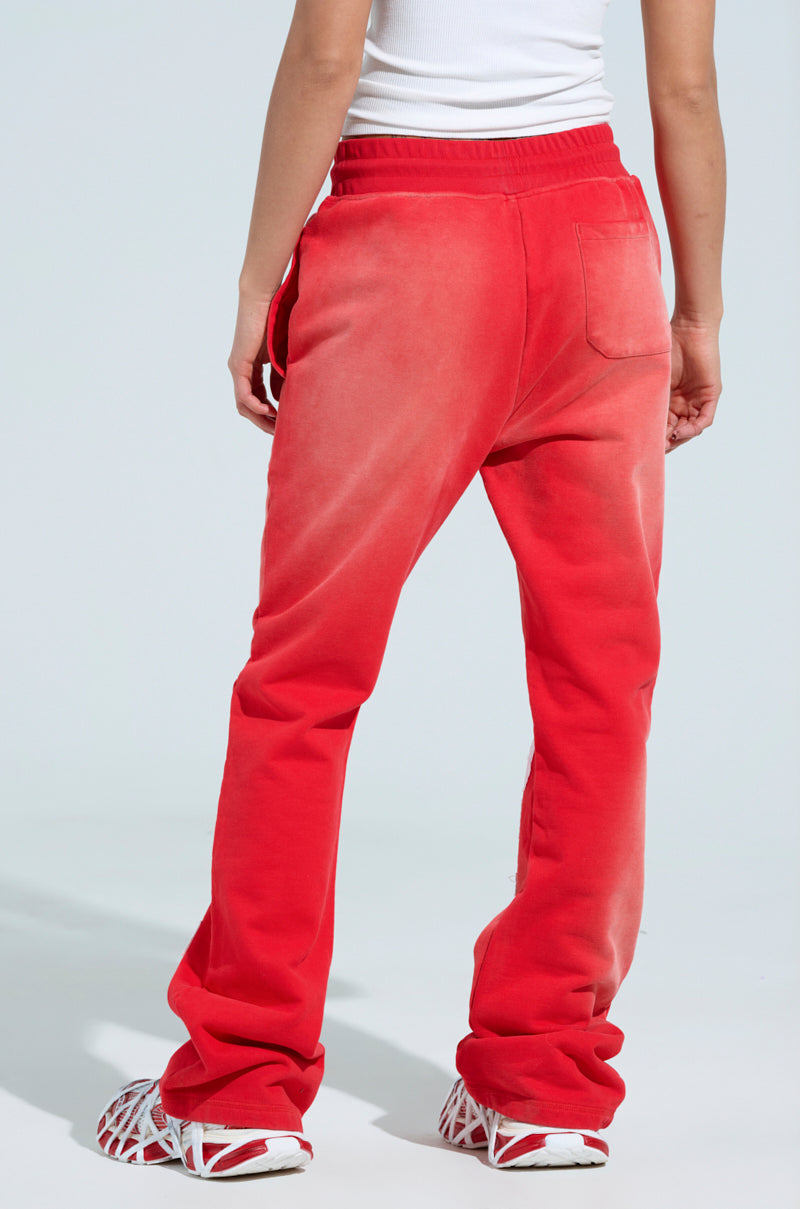 A person models the ONLY ONE WIDE LEG PANT in red, featuring an elastic waistband and white embroidered letter patches. They pair it with a white tank top and matching sneakers against a plain, light background for a casual look. 5