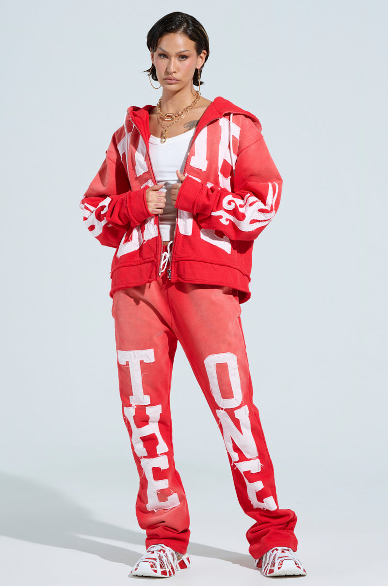 A person wears a red and white tracksuit featuring a zippered hoodie with flame-patterned sleeves and pants showcasing embroidered "ONLY ONE" letter patches and an elastic waistband. They complete the look with white sneakers. 7
