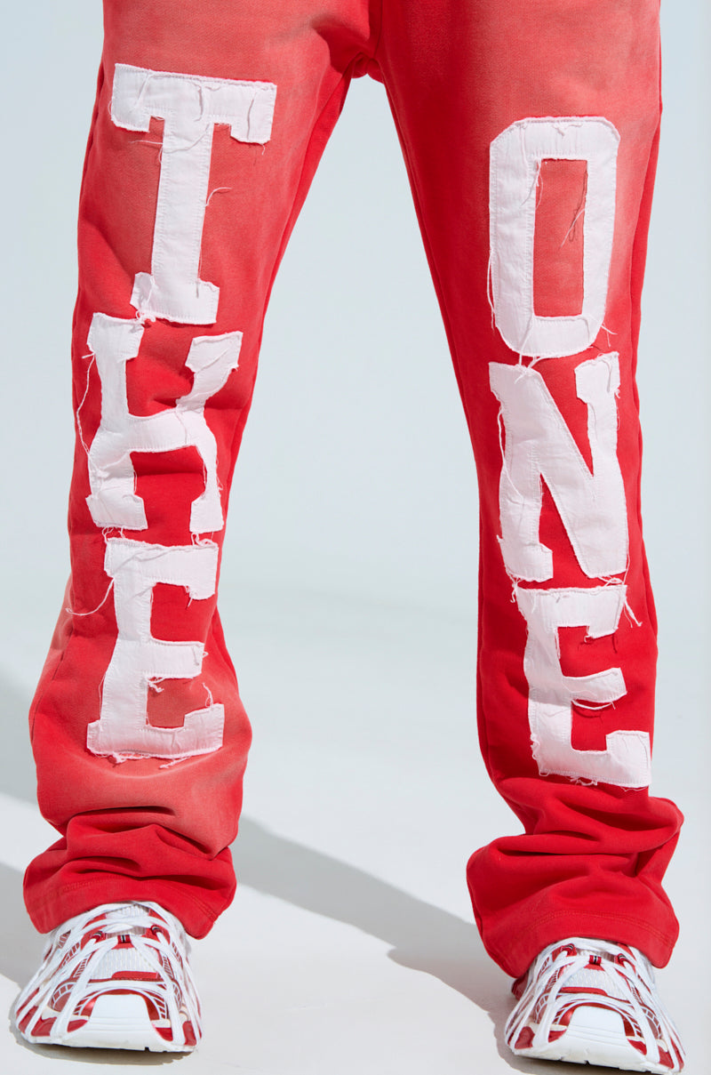 A person wears ONLY ONE WIDE LEG PANT in red, featuring bold white "TAKE ONE" lettering down the legs and an elastic waistband for comfort, paired with white sneakers accented in red. 8