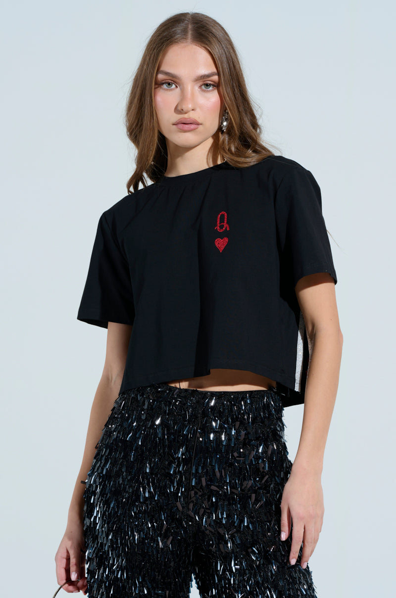 A person with long hair in a LUCKY WINNER T-SHIRT and rhinestone-embellished pants stands against a light background, gazing directly at the camera.