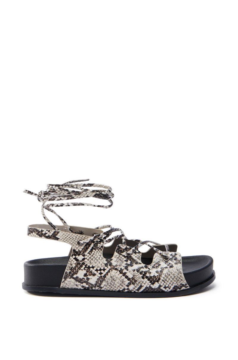 Side view of the AKIRA YUNA RHINESTONE FLOWER EMBELLISHED SANDAL—features a beige multi snake design with black sole, faux snakeskin leather, lace-up vamp, multiple foot straps, and an ankle strap with fringed ties.