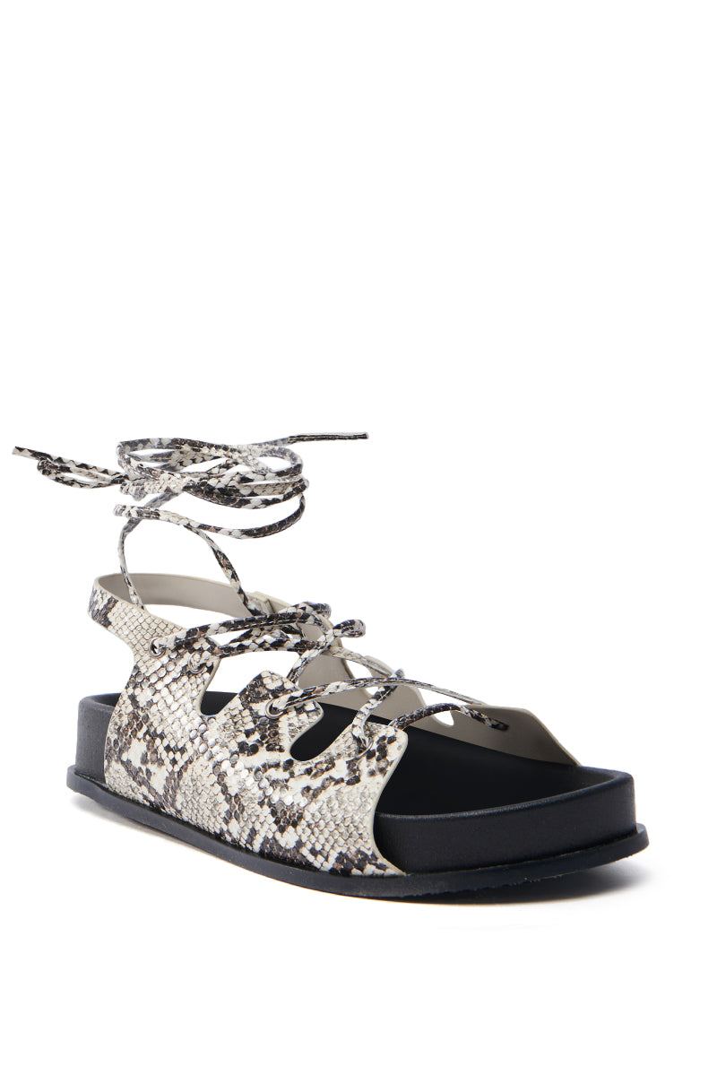 The AKIRA Yuna Rhinestone Flower Embellished Sandal features a black sole, faux-snakeskin pattern, and crisscross laces around the ankle. Its open-toed design with side cutouts adds a casual yet stylish lace-up appeal.