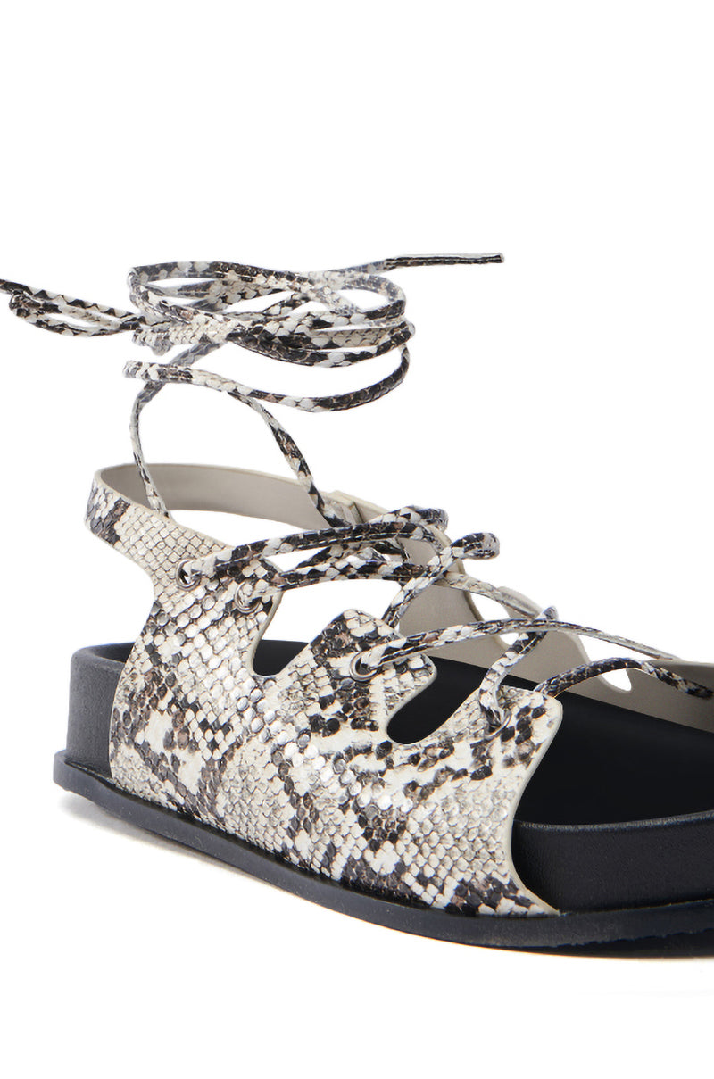 Close-up of the AKIRA YUNA RHINESTONE FLOWER EMBELLISHED SANDAL, featuring a beige multi-snake design with black sole and faux snakeskin leather straps. The sandal highlights an adjustable lace-up vamp that intricately wraps around the ankle.