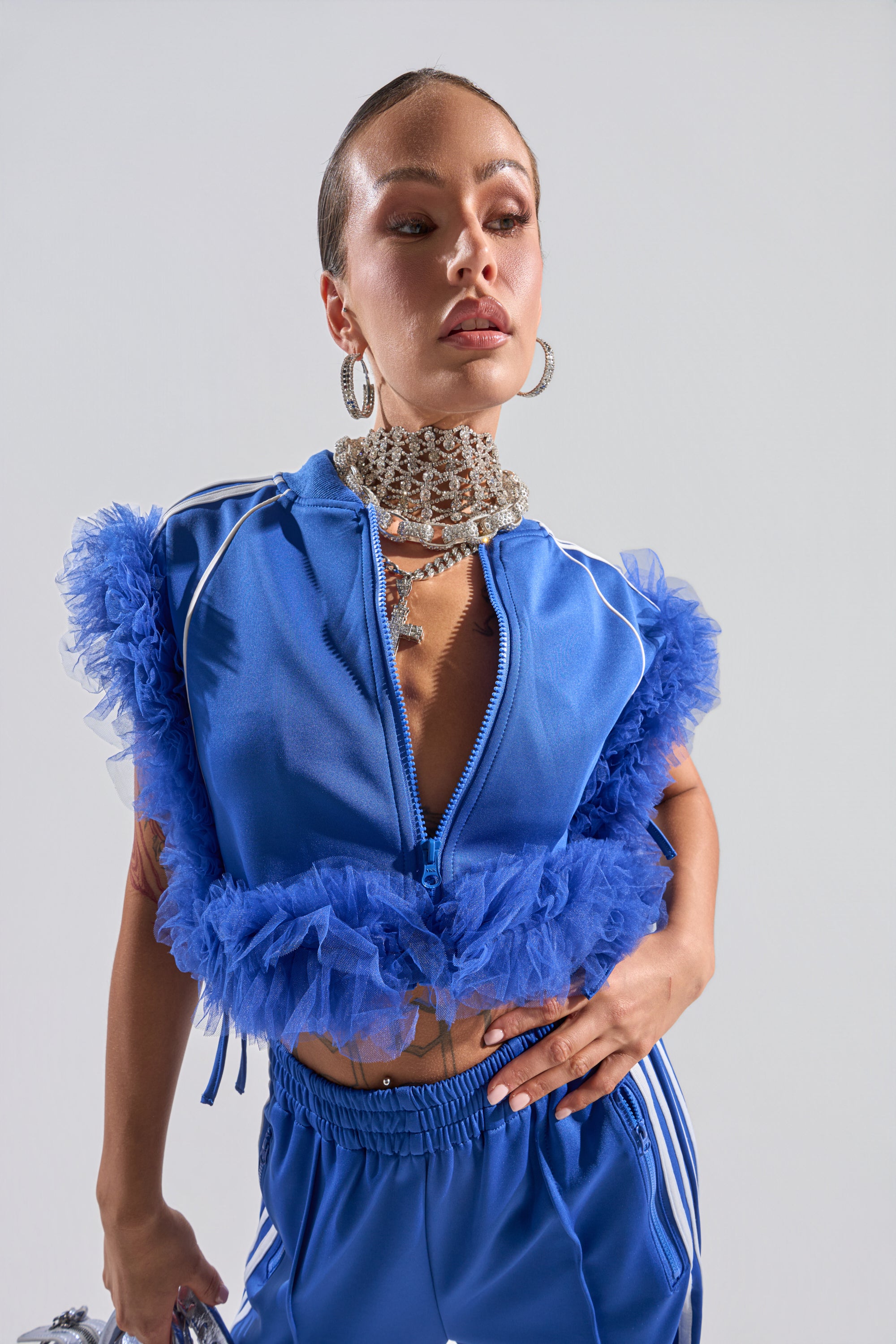 A woman poses confidently against a neutral background wearing the MODERN JAM SWEATSHIRT WITH TULLE IN ROYAL BLUE, styled with large hoop earrings and a statement necklace. 0