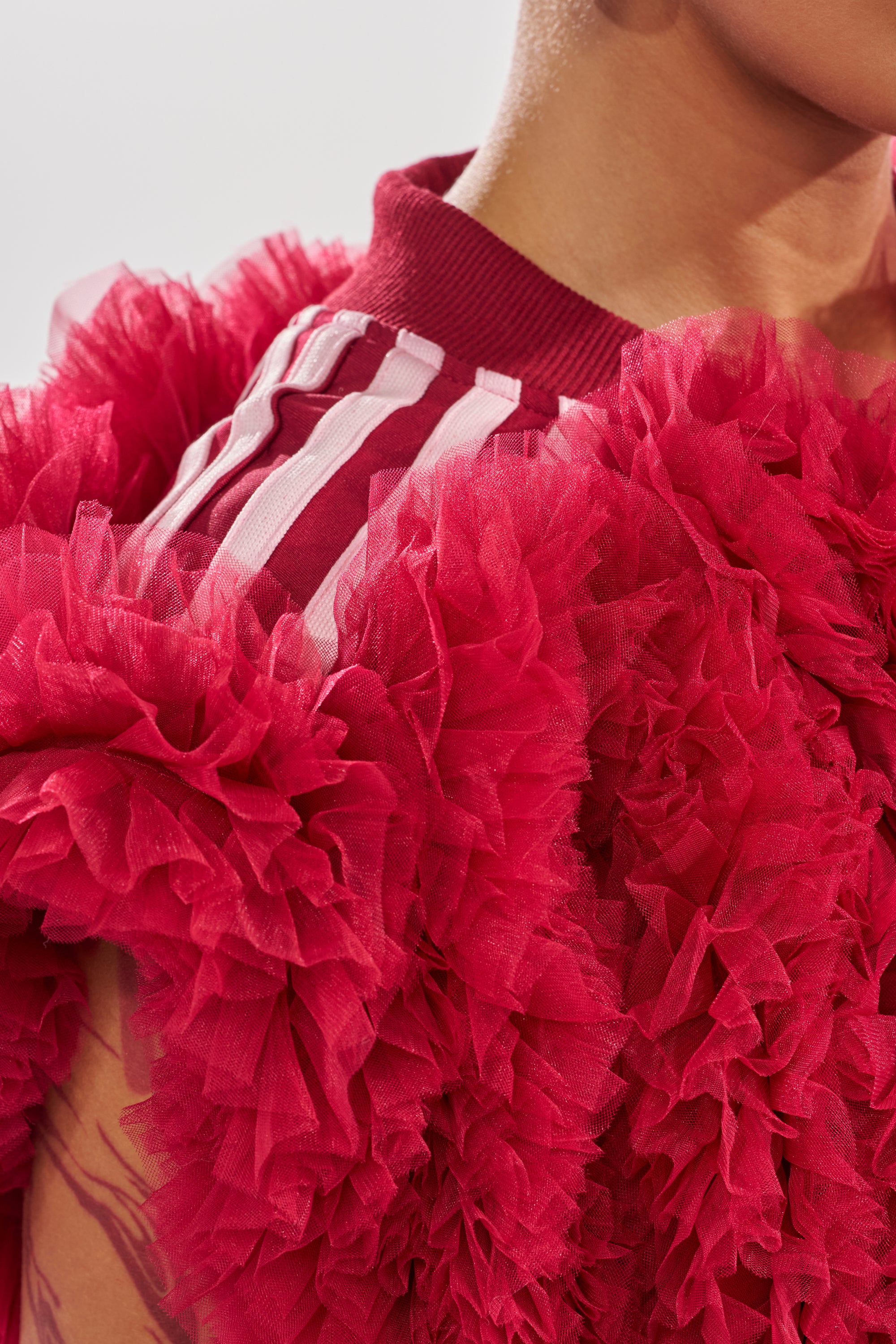 A close-up shows a person wearing the MODERN JAM SWEATSHIRT WITH TULLE IN BURGUNDY, featuring sheer, ruffled layers and white shoulder stripes that accentuate its textured, vibrant athleisure style. 6