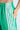 With a relaxed athleisure style, someone models the JUMP AROUND WIDE LEG JOGGER IN GREEN, featuring white vertical stripes. One hand rests in their pocket, accentuating the elastic waistband and revealing a tattoo just above these trendy pants.