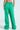 A person wearing the JUMP AROUND WIDE LEG JOGGER IN GREEN stands with their back to the camera. The joggers, featuring an elastic waistband, are paired with white sneakers for a relaxed athleisure look against a light, neutral background.