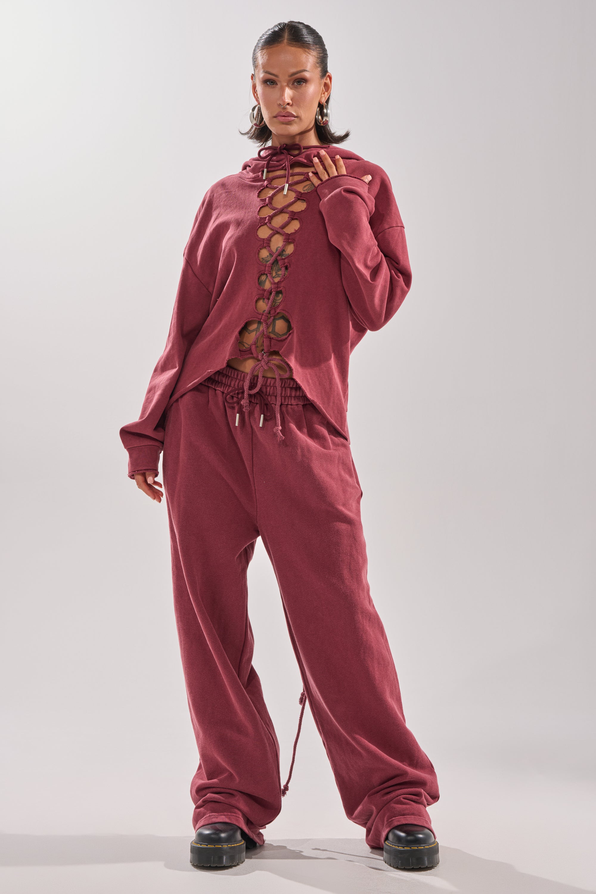 A woman stands confidently in the LACED UP FOR GOOD JOGGER IN PLUM, paired with matching wide-leg pants and black chunky shoes, posing against a plain light background.