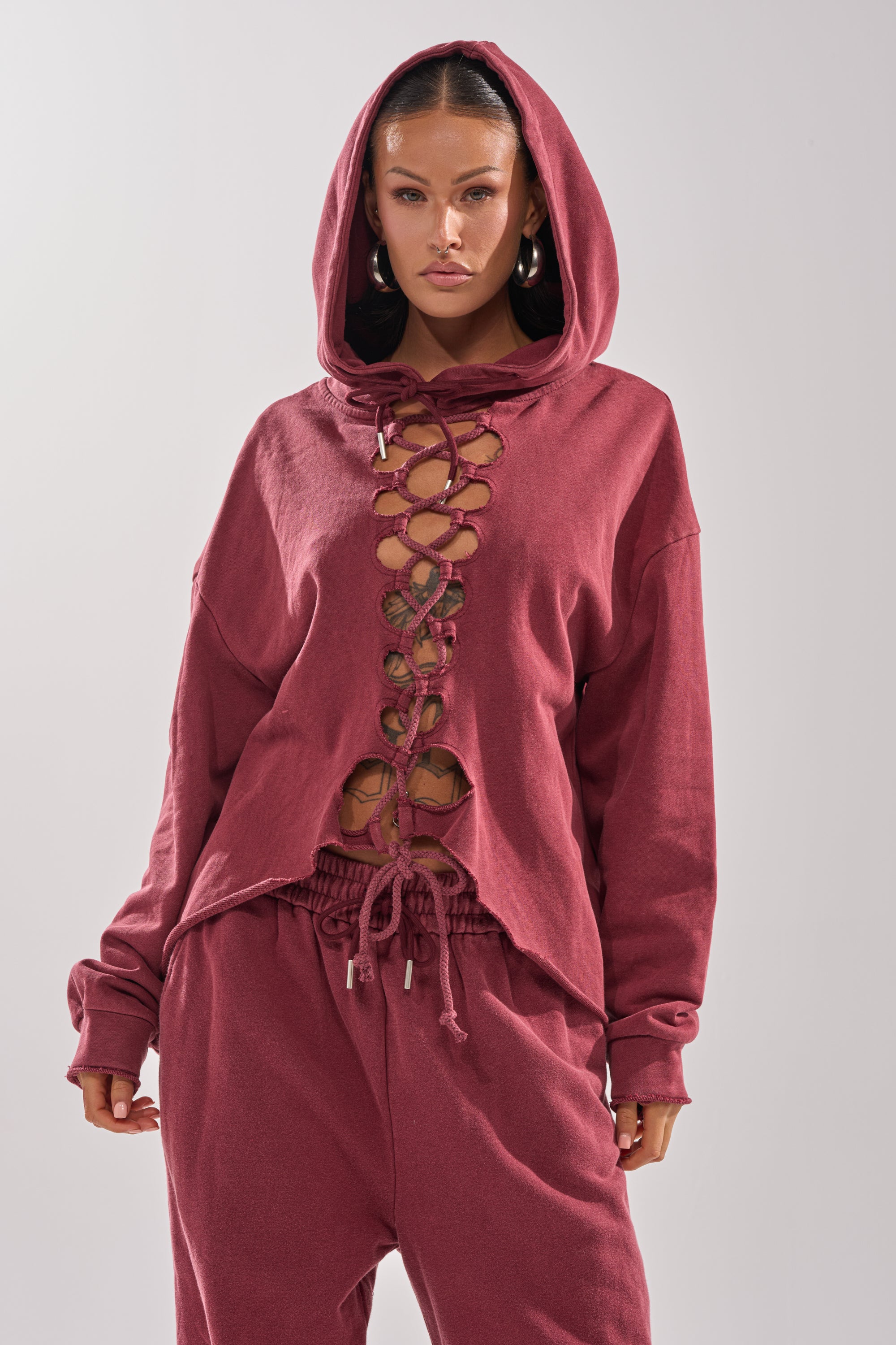 A woman stands against a plain light gray background wearing the LACED UP FOR GOOD SWEATSHIRT IN PLUM with matching sweatpants.