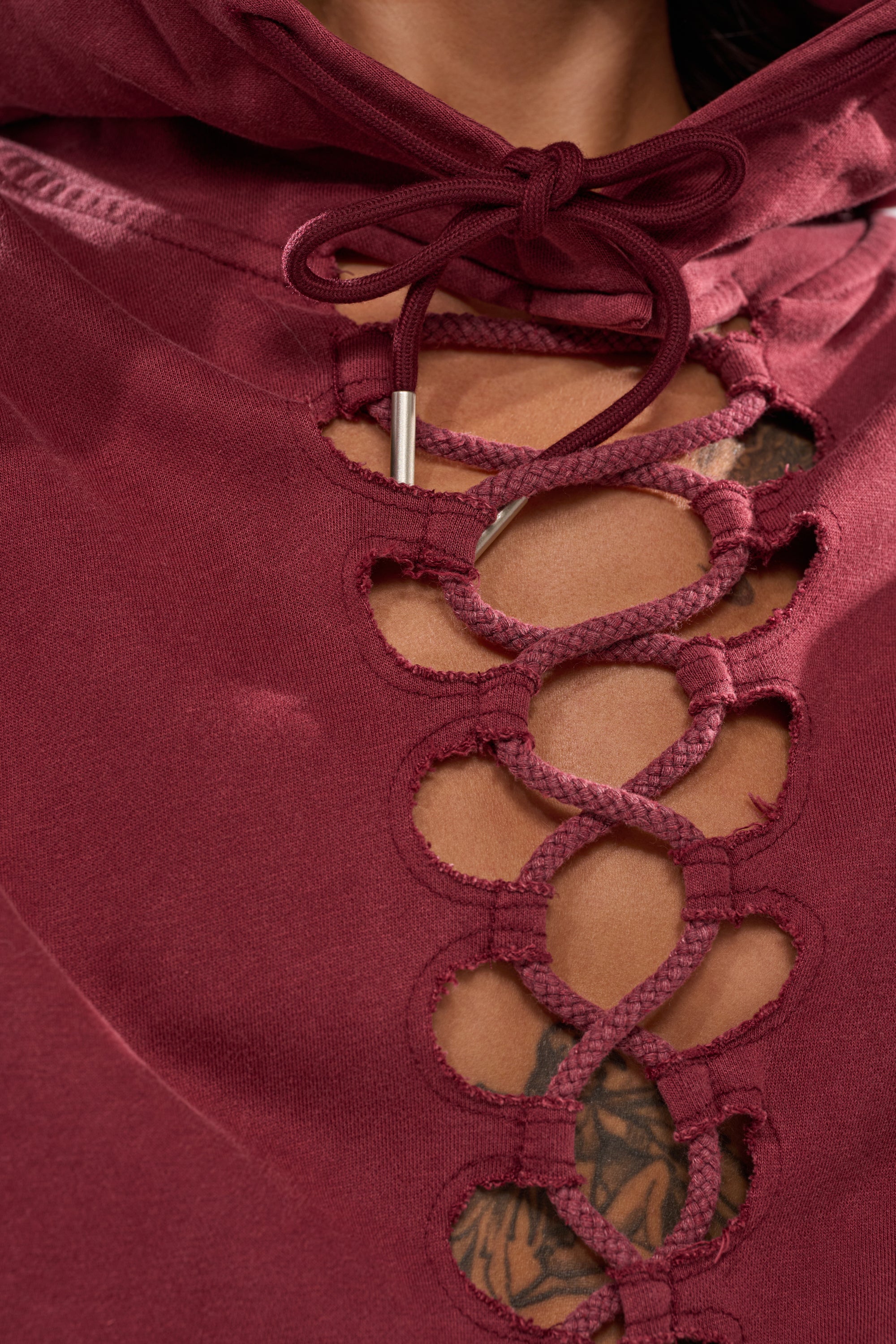 Close-up of a person wearing the LACED UP FOR GOOD SWEATSHIRT IN PLUM, featuring oversized fit and crisscross lacing at the chest that slightly reveals a tattoo beneath.