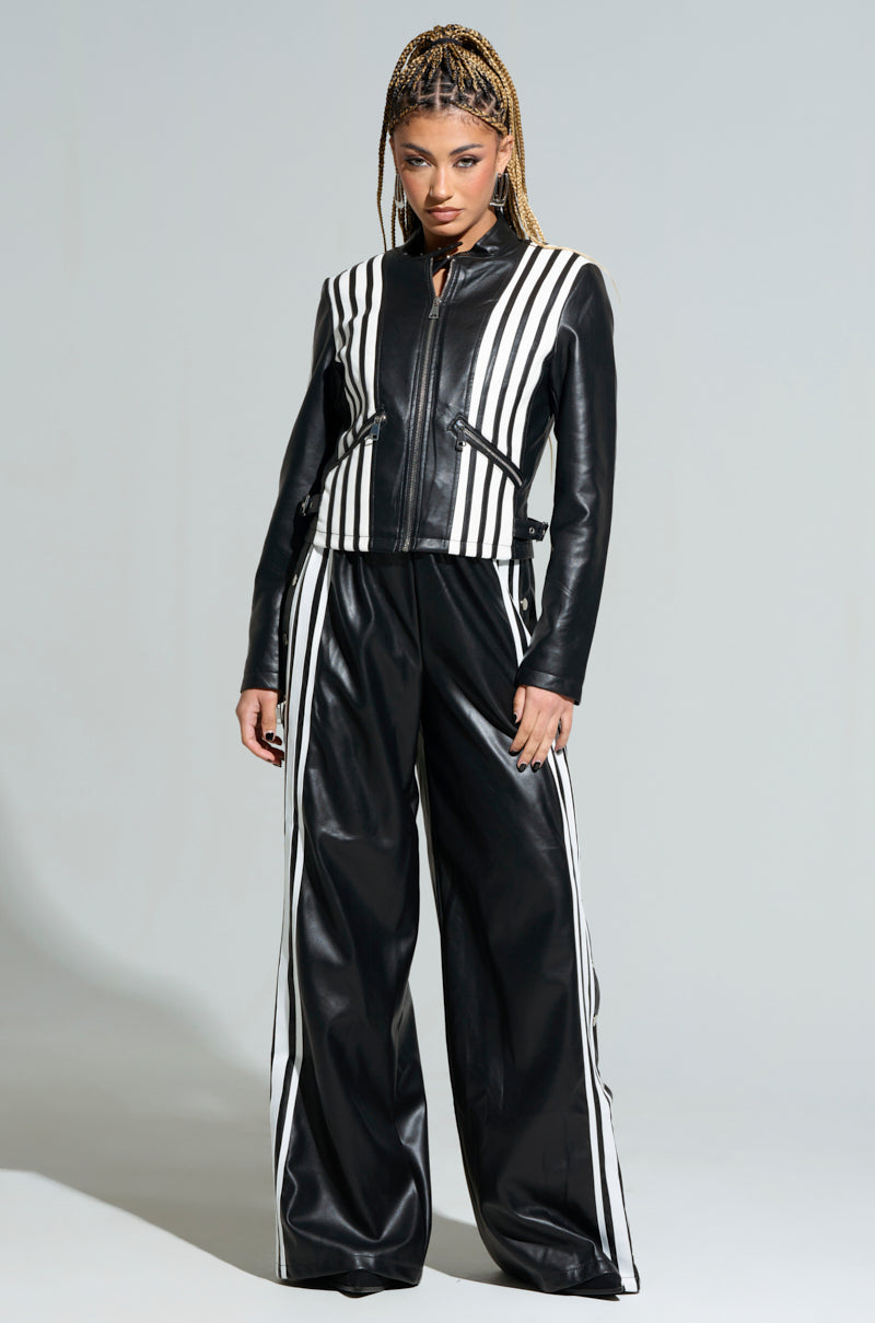 A person wearing the SEE YOU NEXT YEAR PU JUMPSUIT poses confidently, showcasing its stylish design with bold white stripes. They have braided hair and are set against a plain background, highlighting a modern and edgy fashion look.