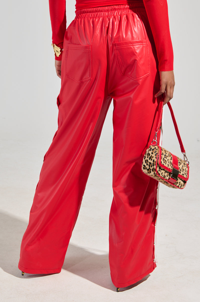 Wearing the BELLERS PANT IN RED and a matching long-sleeve top, a person holds a handbag with leopard print and red accents. The plain light gray background emphasizes the striking, 90's-inspired tearaway look.