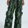 Person wearing the RUNNIN WILD CARGO PANT in a sleek green and black snakeskin pattern, featuring multiple pockets and button details. These faux leather pants boast a shiny, textured surface for a bold look.