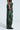 A person wearing the RUNNIN WILD CARGO PANT, which features a snakeskin pattern in green faux leather with multiple pockets and a textured appearance, pairs it with a lace top while standing against a plain background.