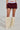 Against a neutral backdrop, a person wears a white mesh top, maroon puffy shorts with a bubble hem reminiscent of the Varsity Squad Bubble Mini Skirt, fuzzy beige leg warmers, and white pointed shoes, highlighting their lower half.