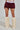 Someone displays maroon balloon shorts, echoing the Varsity Squad Bubble Mini Skirt, alongside fluffy cream leg warmers worn over white pointed shoes, all set against a plain light gray background.