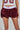 A person wearing a mesh sports top and the VARSITY SQUAD BUBBLE MINI SKIRT in burgundy, featuring a white elastic waistband and glossy windbreaker-like texture with 
