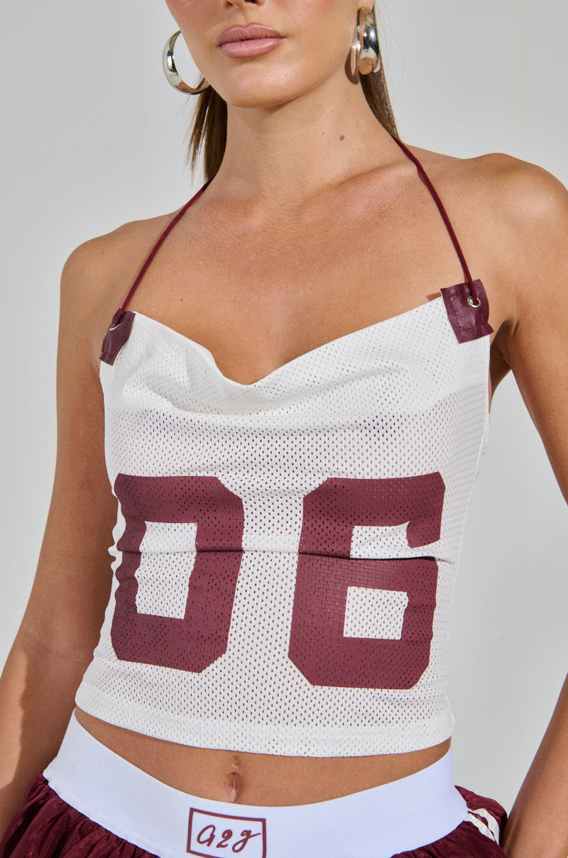 Sport a chic look with a white mesh halter top featuring maroon "06," reminiscent of the VARSITY SQUAD TANK, complemented by large hoop earrings and maroon shorts with a white waistband. 6